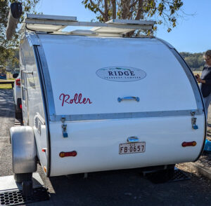 Teardrop camper trailer photographed from the rear with solar panels on the roof and a retractable awning on the left