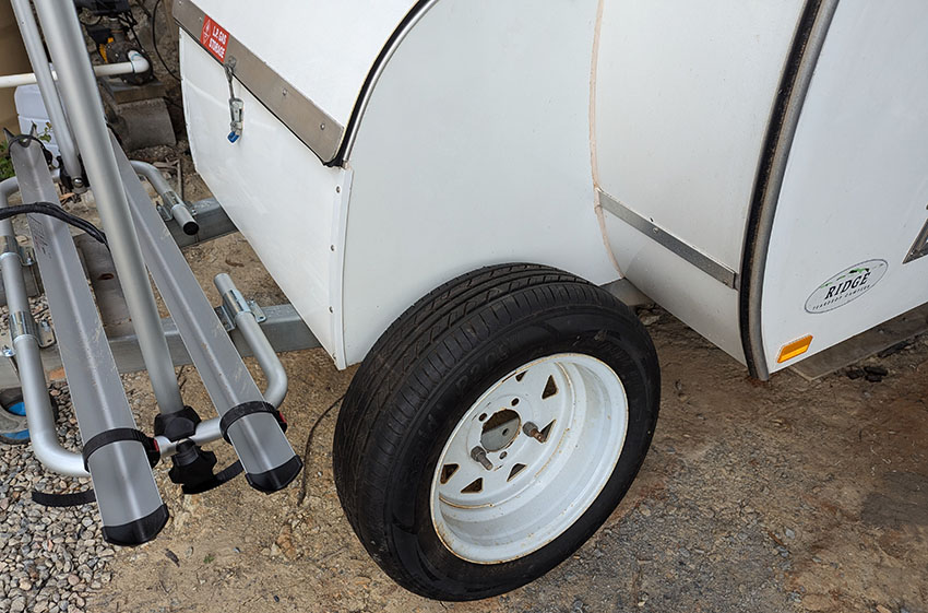 Photo of spare wheel on the ground next to the toolbox on the tongue of the camper