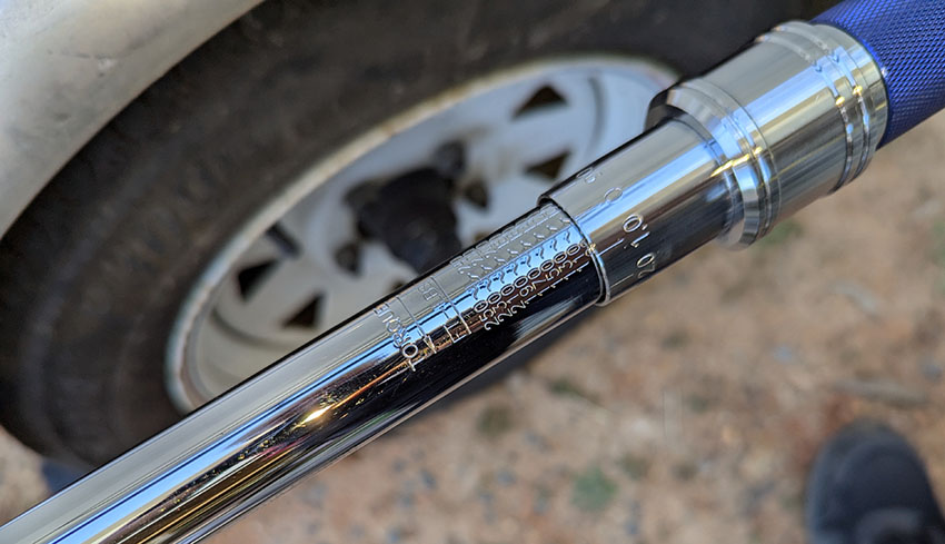 Torque wrench in the foreground with an RV trailer wheel in the blurred background